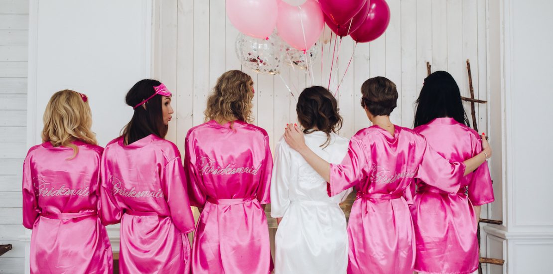 Back view of group of bridesmaids with bride-to-be in beautiful silk robes with different names on their backs.