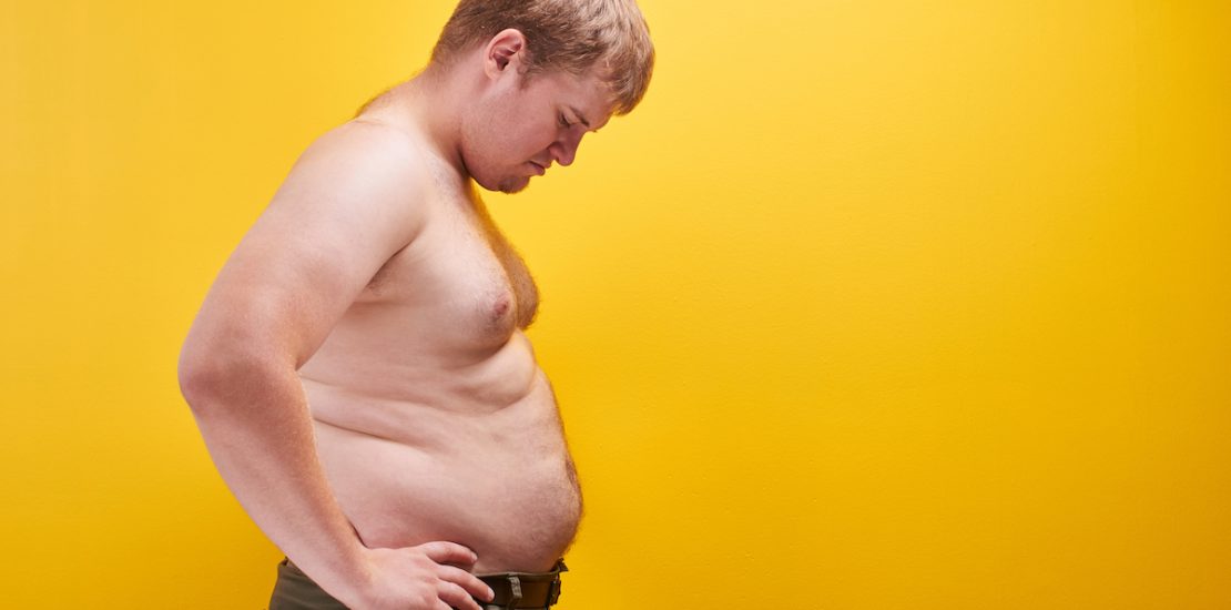 Huge young man with big fat belly and naked body in profile. Concept of obesity, fast and junk food, sports, liposuction, weight loss with free space for your product or text