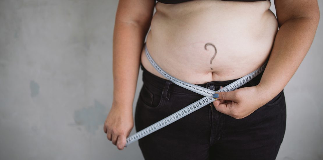 Overweight woman measuring waist with measure tape, close up image. Weight loss, motivation, fat burning