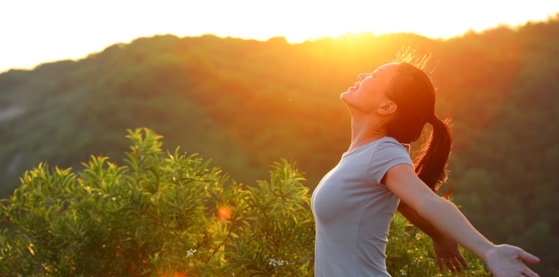 cheering woman open arms at sunrise mountain peak wellness concept