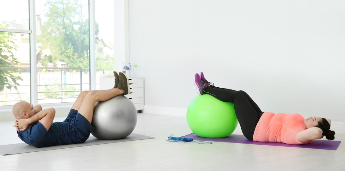 Overweight man and woman doing exercise with fitness balls in gym