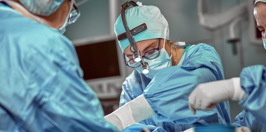 Portrait of team of multiethnic surgeons at work in a operation theatre. Several doctors surrounding patient on operation table during their work. Team surgeons at work in operating room.