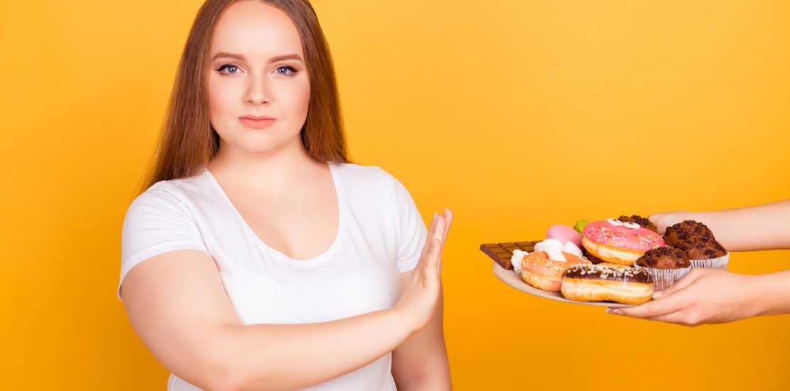 I'm against eating products containing fat! Will-powered woman wearing white tshirt is refusing to consume tasty delicious sweets on a plate, isolated on bright yellow background
